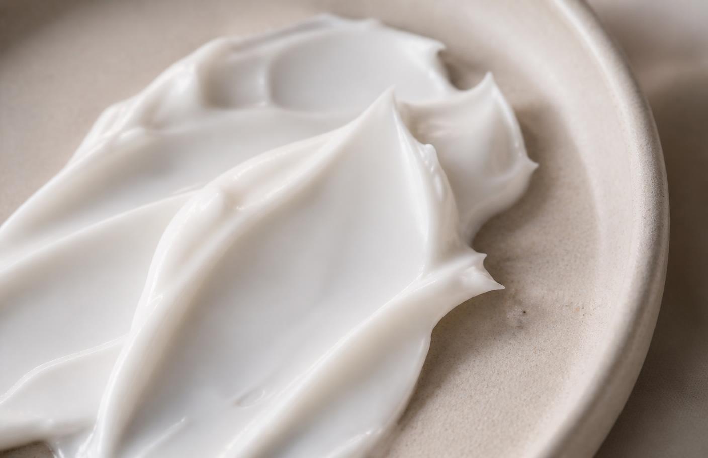 Close-up texture shot of a rich white ceramide barrier moisturiser swatched in soft peaks on a pale oat ceramic dish